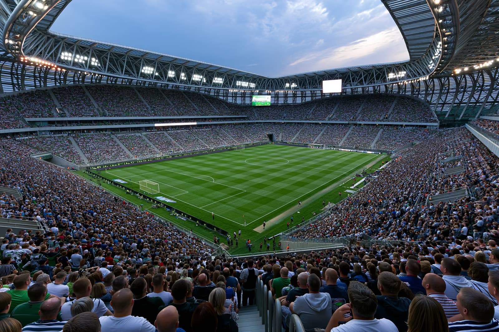 Un grande stadio di calcio gremito di tifosi sotto i riflettori in una sera d'estate.
