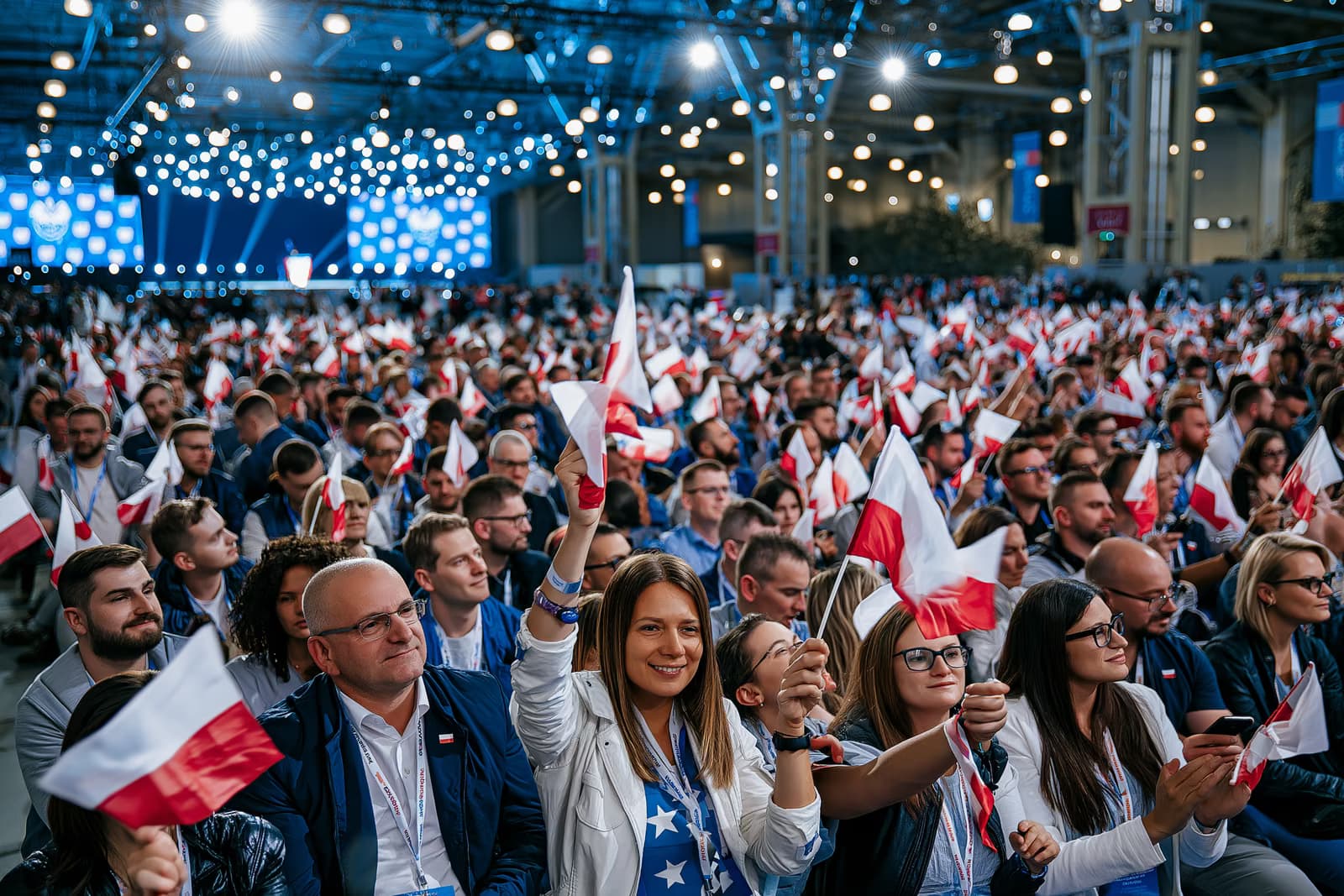 Una folla gremita nella sala espositiva sventola piccole bandiere sotto le luci intense dell'evento, in occasione del lancio della campagna elettorale dell'AfD a Magdeburgo, con un palco sullo sfondo.