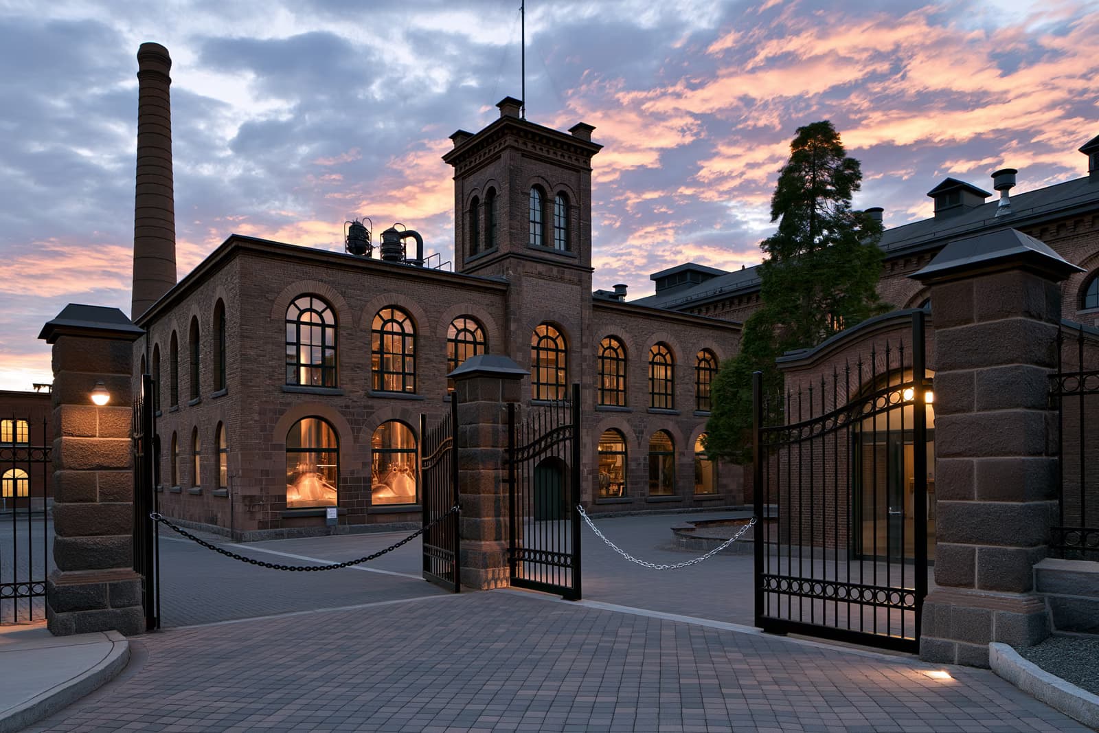 Al tramonto, dietro cancelli incatenati, si erge un edificio storico che ospitava un birrificio, con le caldaie di rame visibili attraverso finestre ad arco, a segnare la fine del birrificio Eichbaum.