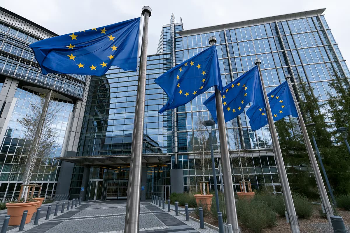 Bandiere dell'Unione Europea su aste portabandiera di fronte a un moderno edificio in vetro.